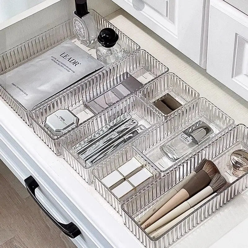 Clear plastic drawer organizers with makeup items in a white cabinet.